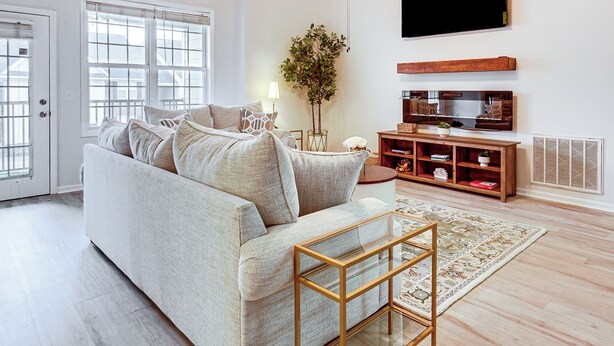 A modern living room with a sofa, a TV, a wooden TV stand, a floor lamp, and a large window. - 9 Mi to Dtwn Fayetteville: Condo w/ Pool Access! (Fayetteville)