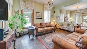 A spacious living room with leather sofas, a chandelier, and a large potted plant.