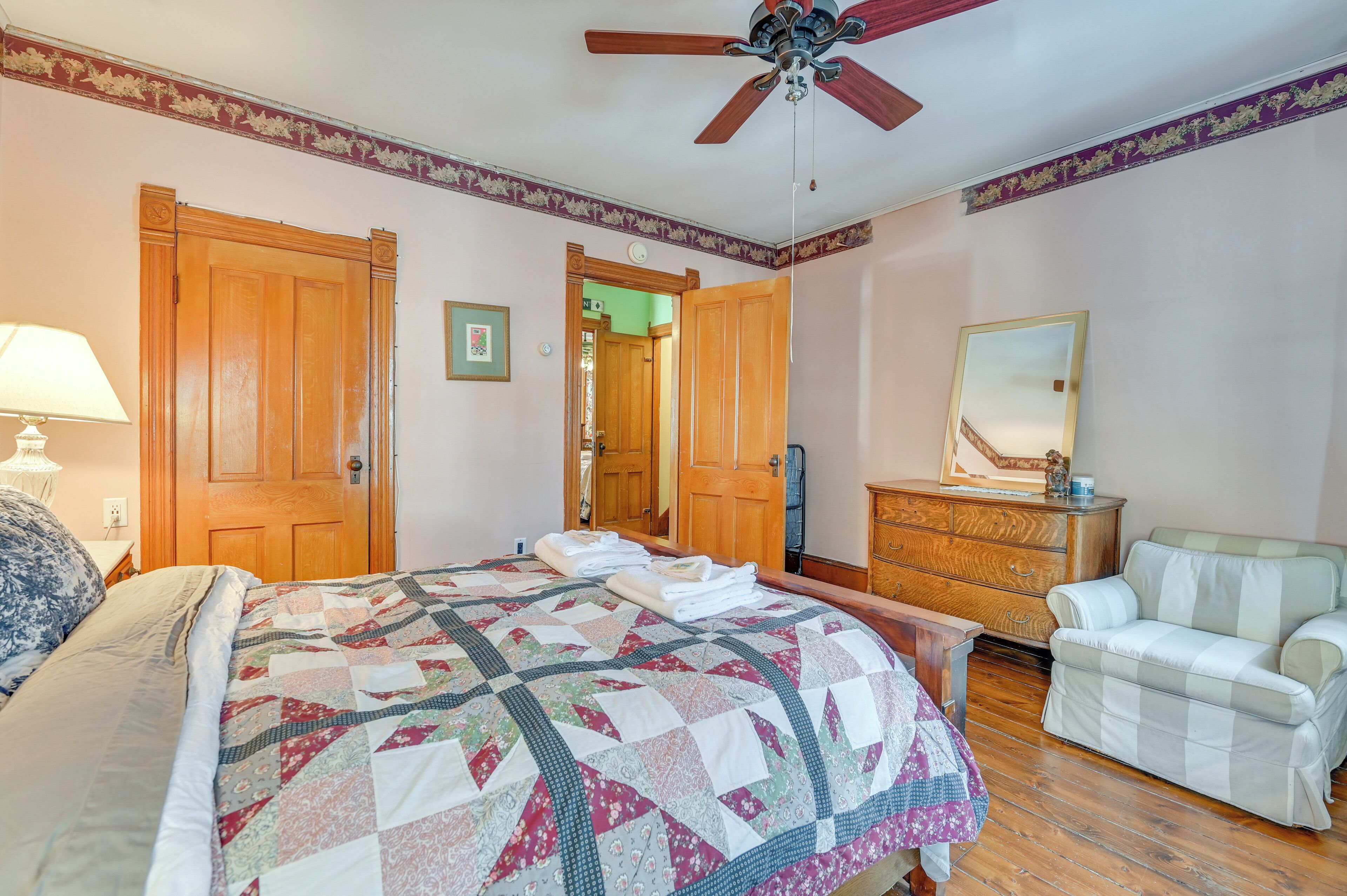 A bedroom with a large bed, wooden wardrobe, a dresser, a chair, and a ceiling fan.