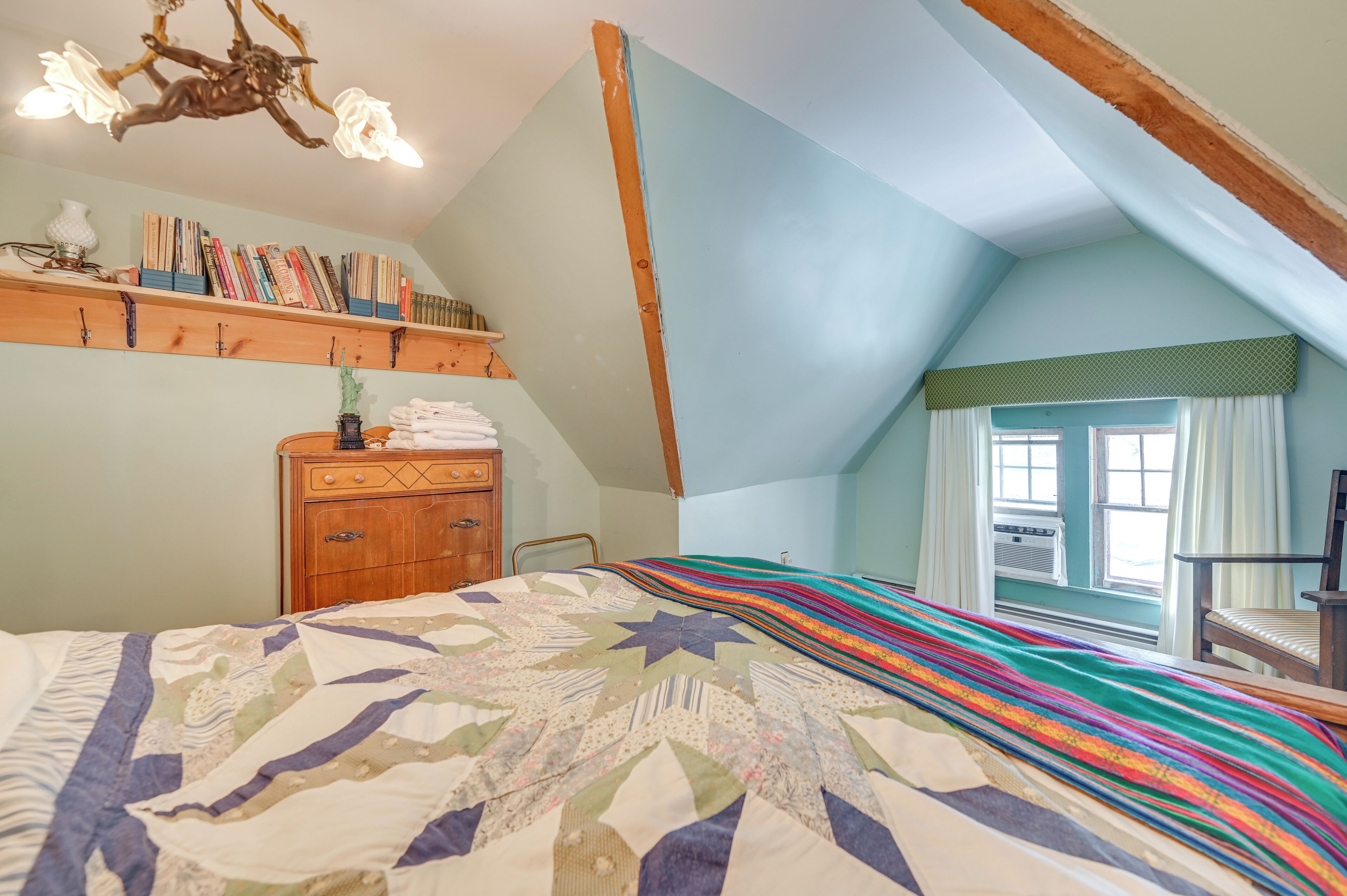 A bedroom with a large bed, a wooden dresser, a bookshelf, and a window with curtains.