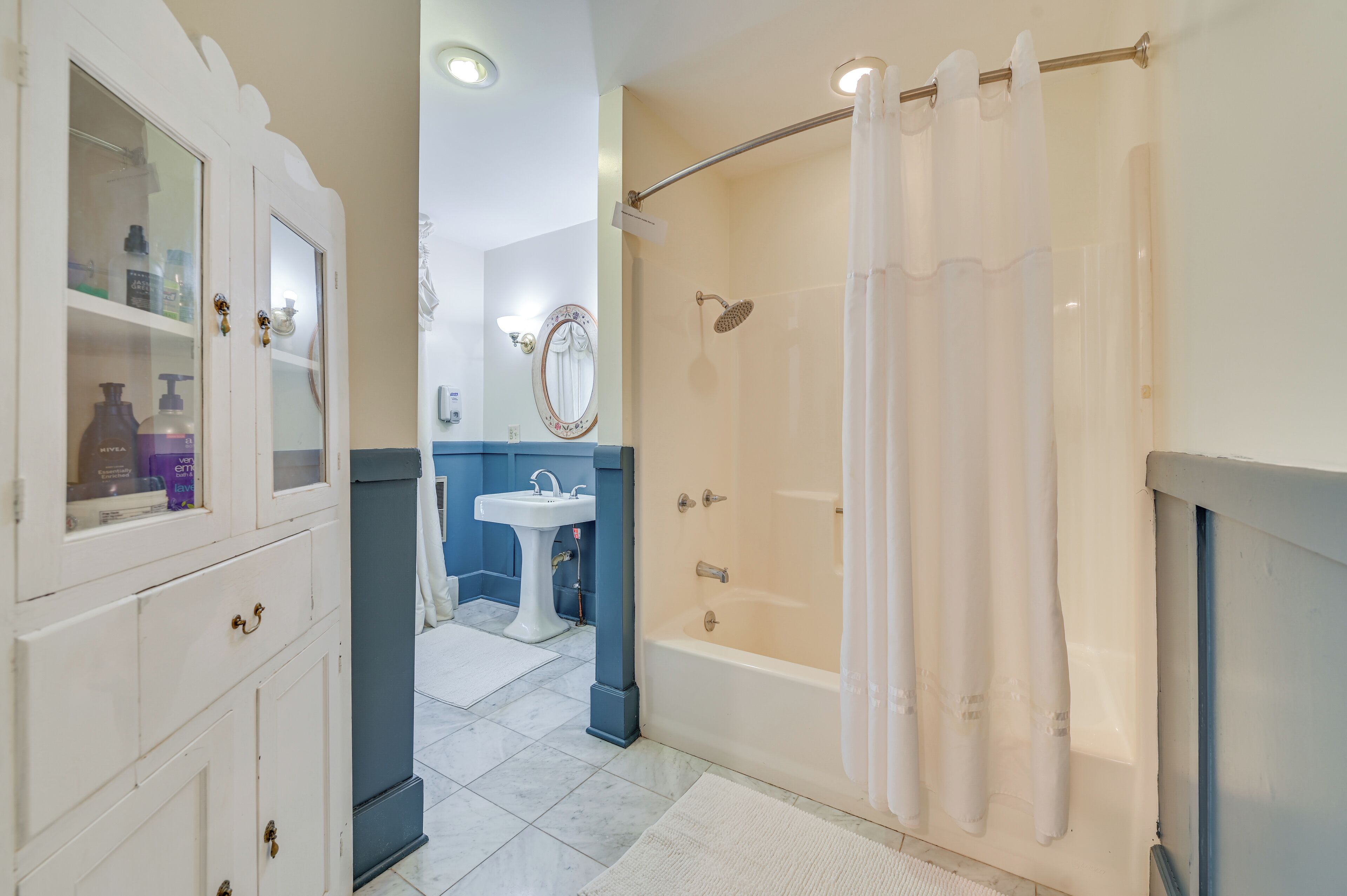 A bathroom with a bathtub, a shower, a sink, and a cabinet with glass doors.