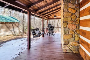A covered wooden deck with stone pillars, a swing, and a table with chairs. - 3 Mi to Dtwn Ellijay: Tree-lined Cabin w/ Deck! (Ellijay)