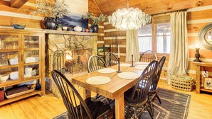 Un interior de madera con una mesa de comedor dispuesta para seis personas, rodeada de sillas, una chimenea de piedra y un candelabro.