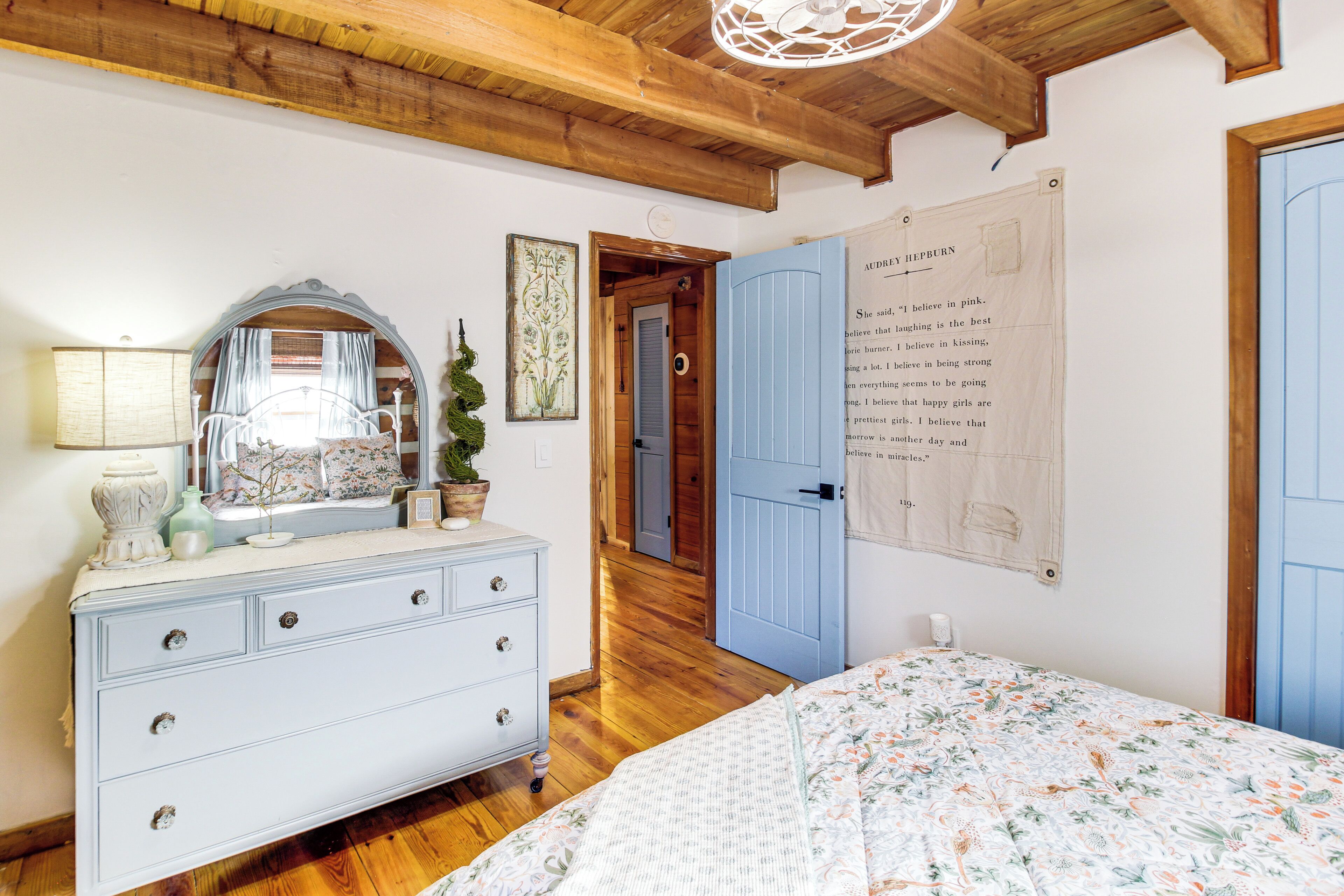 Ein Schlafzimmer mit Bett, Kommode, Spiegel und einem Poster an der Wand.