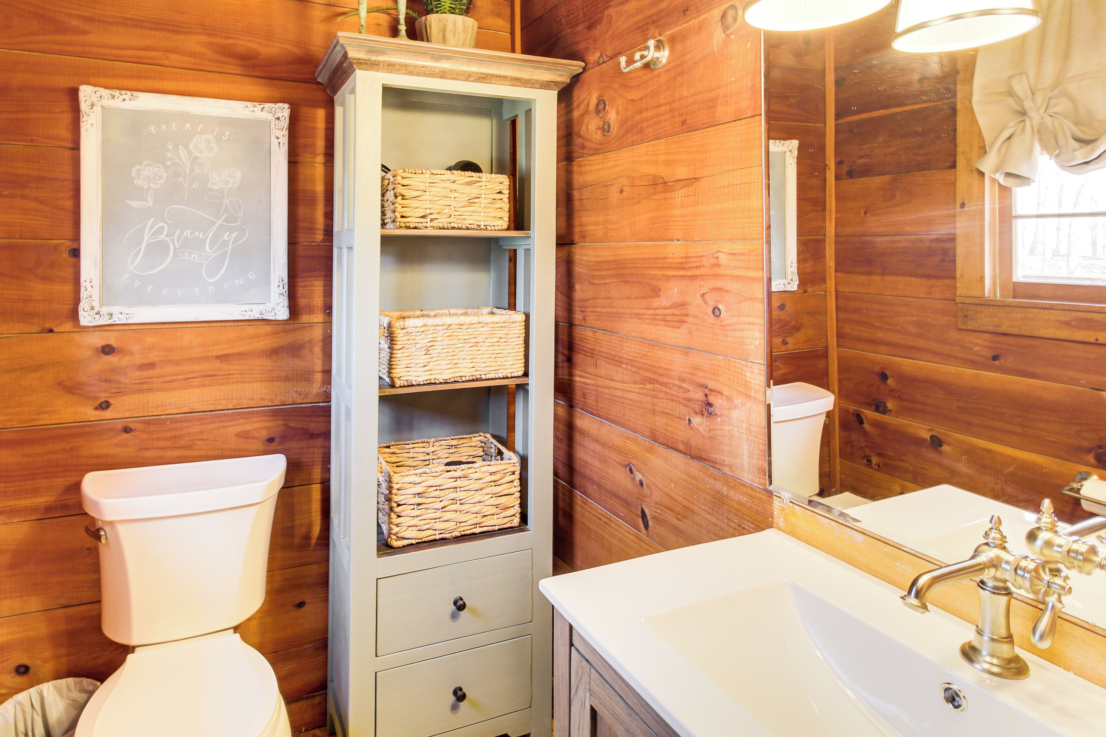 A wooden bathroom with a toilet, a cabinet with wicker baskets, and a sink with a mirror.