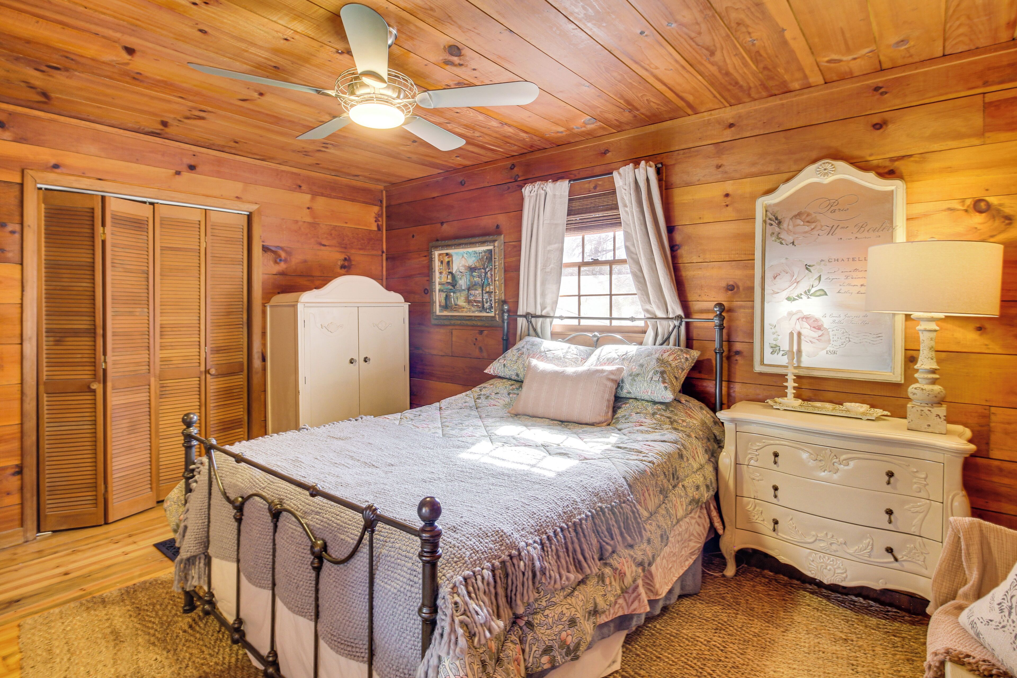 A wooden cabin bedroom with a bed, nightstand, dresser, and a ceiling fan.