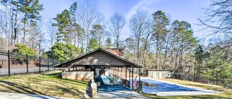 A covered pavilion with a concrete floor, surrounded by trees and a fenced area.