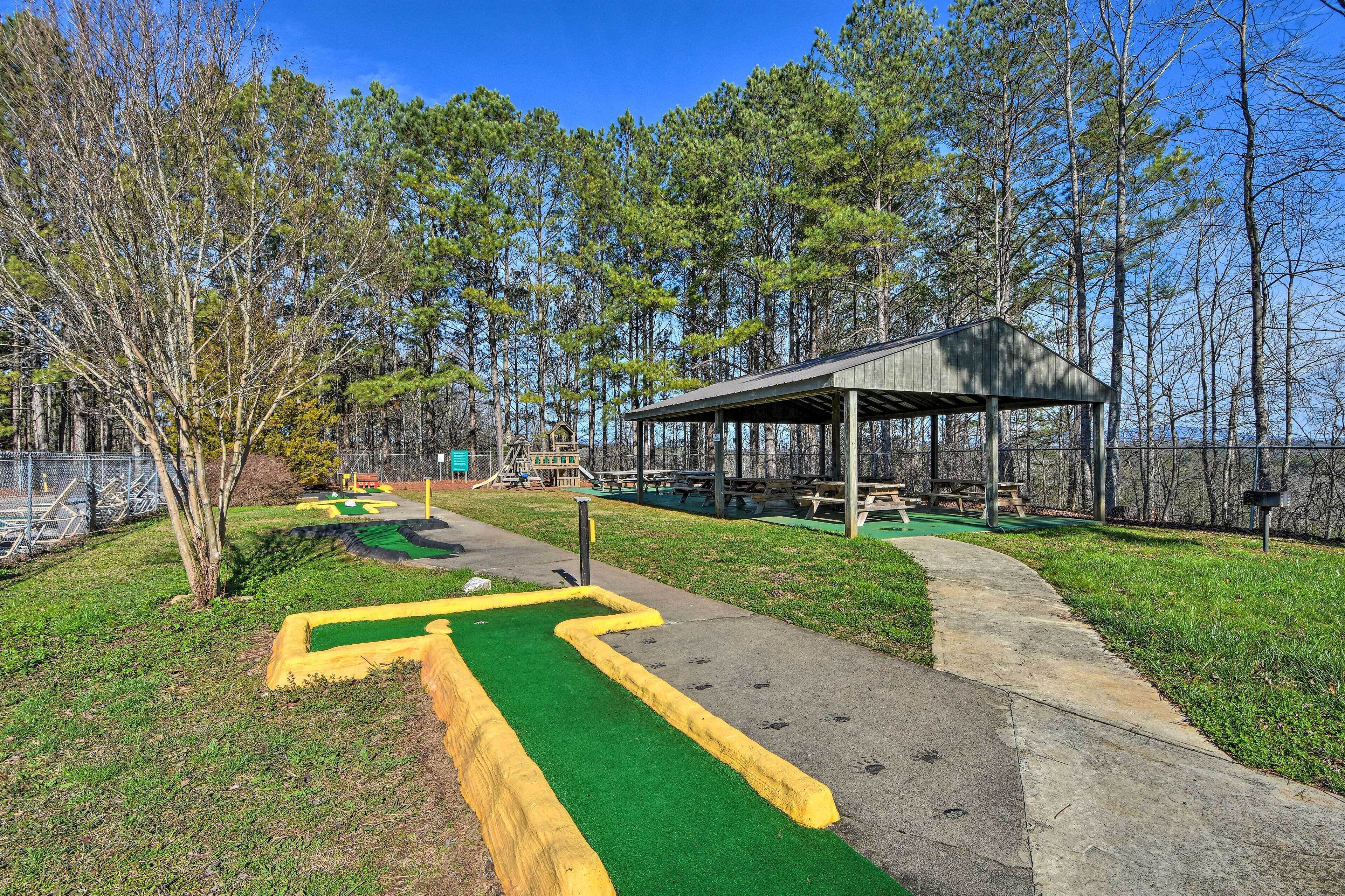 A park with a green walking path, a covered picnic area, and a playground in the background.