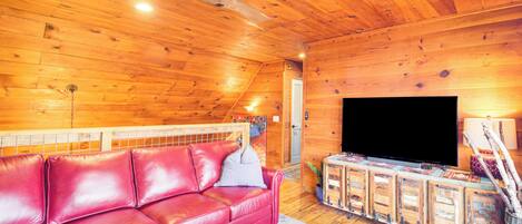 A cozy wooden cabin interior with a red leather sofa, a ceiling fan, and a television.