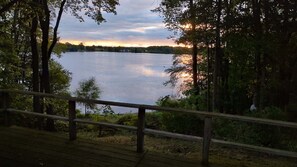 A wooden deck overlooking a calm lake with trees in the background. - Peaceful, Private Lakeside Home. Sleeps 16! (Pentwater)