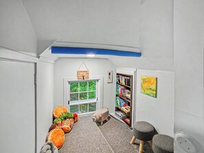 A cozy reading nook with a bookshelf, a plush toy, and a window with a view of greenery. - Peaceful, Private Lakeside Home. Sleeps 16! (Pentwater)