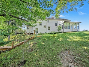 A two-story house with a covered porch, a wooden deck, and a grassy yard.