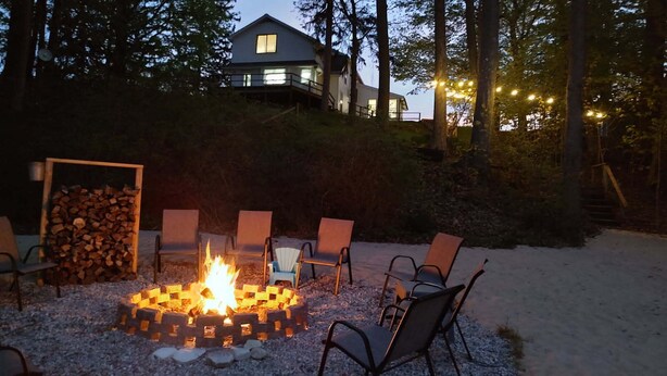 A fire pit surrounded by chairs in a snowy outdoor area, with a house and trees in the background. - Peaceful, Private Lakeside Home. Sleep 16! (Pentwater)