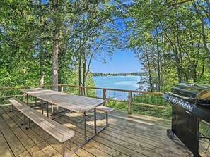 A wooden deck with a picnic table and a barbecue grill overlooking a lake. - Peaceful, Private Lakeside Home. Sleeps 16! Available for monthly rental! (Pentwater)