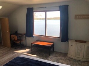 A room with a bed, a desk, a chair, a window with curtains, and a view of a body of water. - Peaceful, Private Lakeside Home. Sleeps 16! (Pentwater)