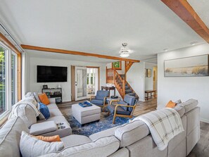 A spacious living room with a large sofa set, a coffee table, and a staircase leading to another room. - Peaceful, Private Lakeside Home. Sleeps 16! (Pentwater)