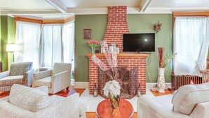 Ein Wohnzimmer mit Kamin aus Ziegelsteinen, einem flachbildfernseher darüber und unterschiedlichen Sitzgelegenheiten, darunter Sofas und Sessel.