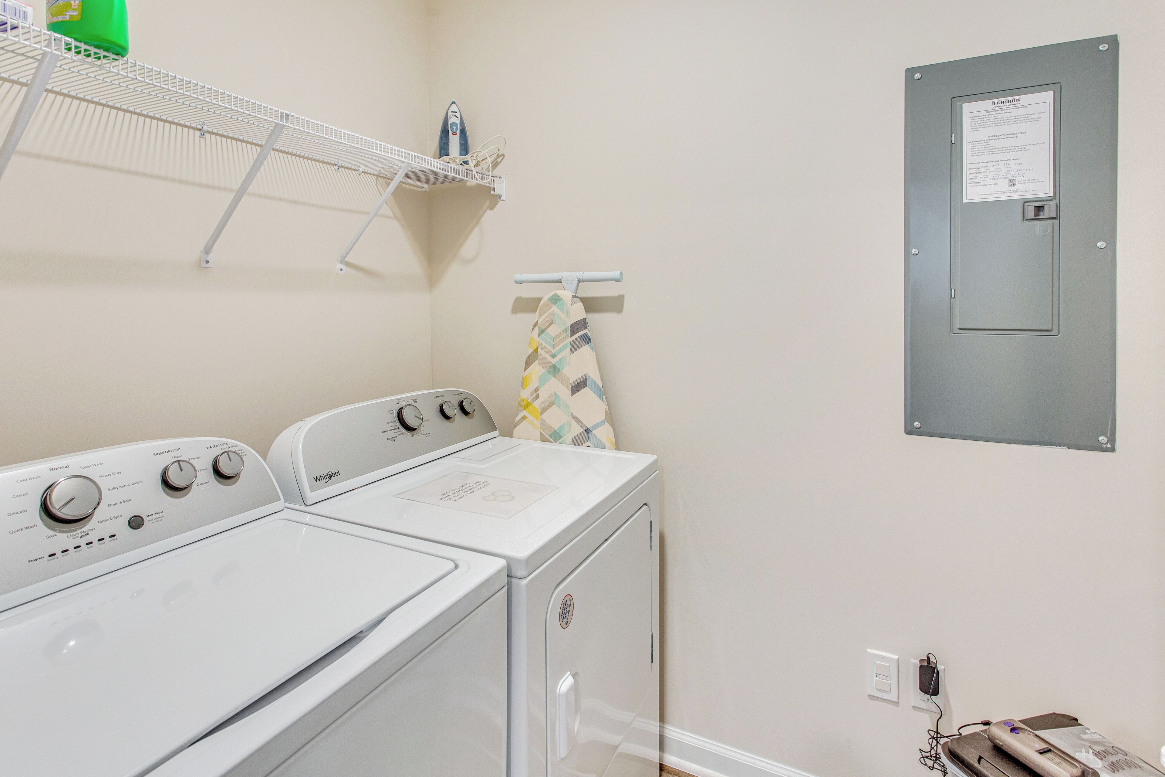 Uma lavanderia com máquina de lavar e secadora empilhadas, uma prateleira com produtos de limpeza e uma porta de serviço com uma placa.