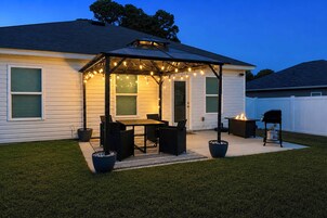 A covered patio area with a table and chairs, a fire feature, and a grill.