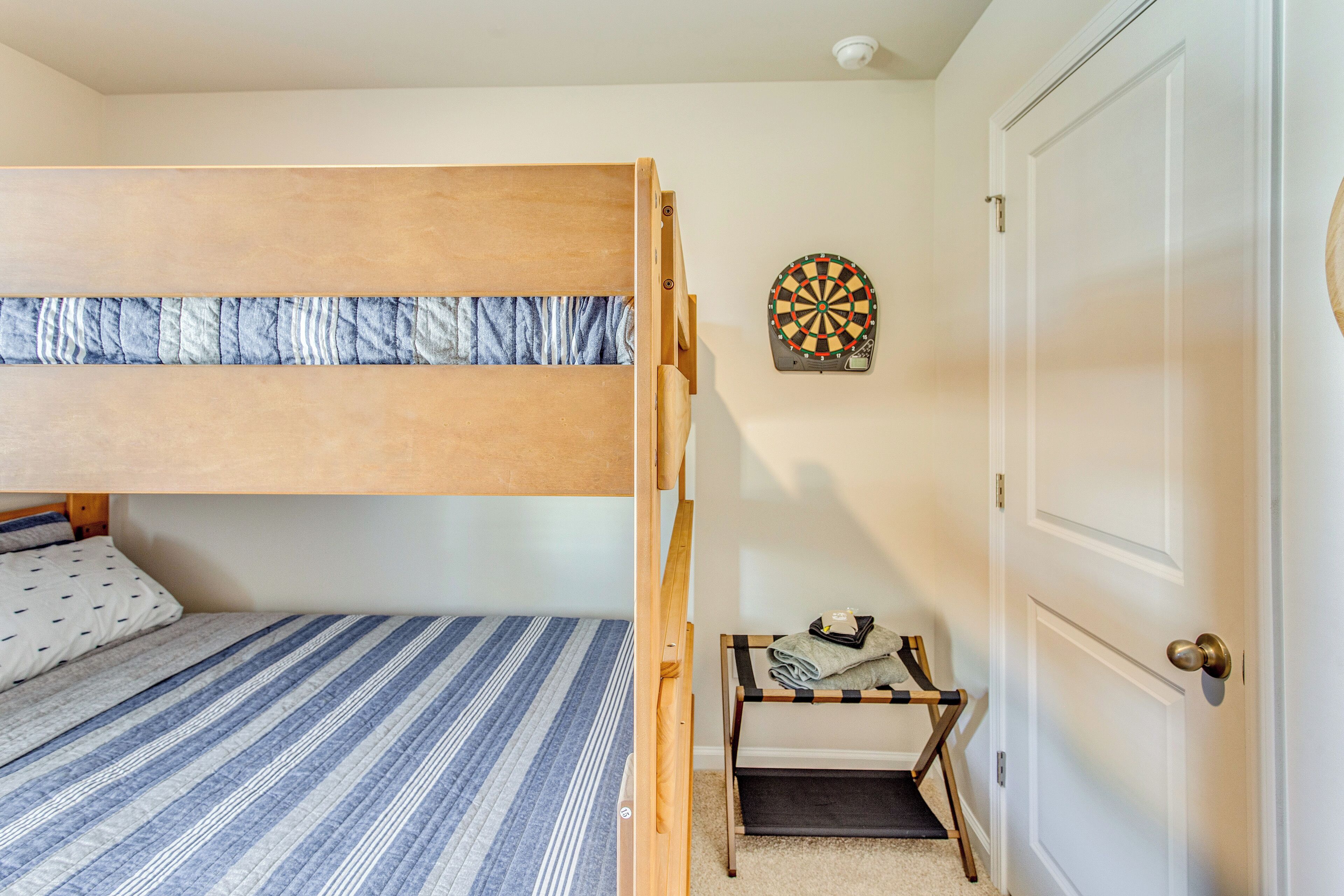 A bunk bed with a striped mattress, a dartboard on the wall, and a small table with folded towels.