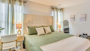 Ein Schlafzimmer mit einem Bett, zwei Nachttischen, einem Sessel, einem Deckenventilator und einem großen Fenster mit Vorhängen.