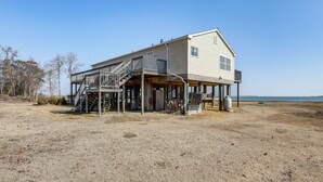 Uma casa de dois andares com varanda e alpendre, localizada na praia de areia com vista clara para o oceano.