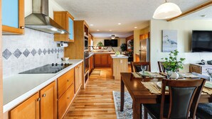 Uma cozinha moderna com armários de madeira, exaustor de aço inoxidável e uma área de jantar com mesa e cadeiras de madeira.
