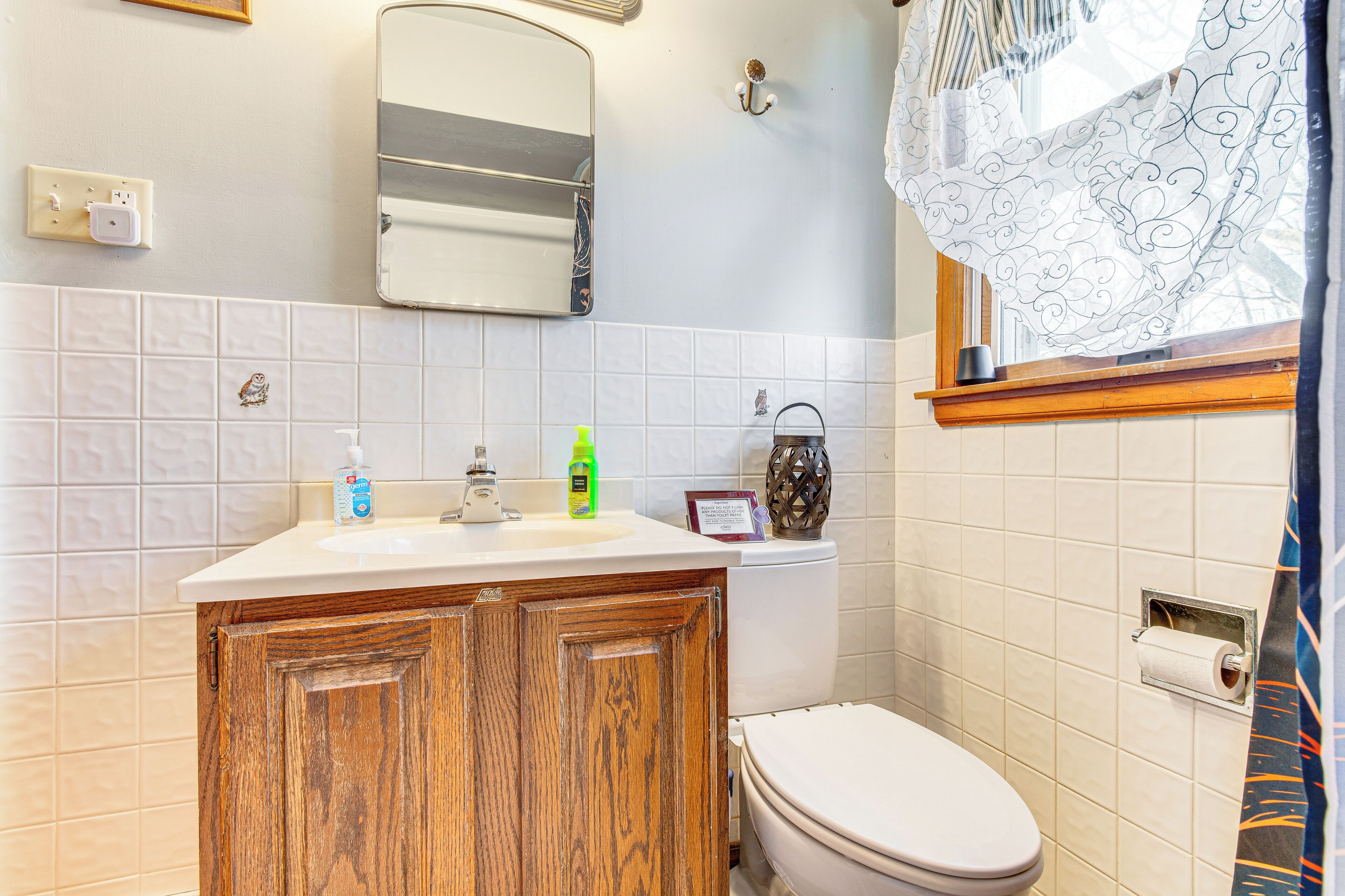 A bathroom with a wooden cabinet, a white toilet, a mirror, and a window with a curtain.