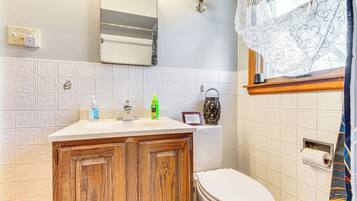 A bathroom with a wooden cabinet, a white toilet, a mirror, and a window with a curtain.