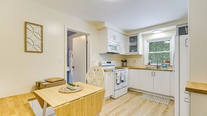 A compact kitchen with white cabinets, a microwave, an oven, and a sink. There's a wooden dining table and a chair. - Near Detroit Metro Area: New Baltimore Home! (New Baltimore)