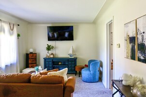 Una sala de estar con un sillón azul, un sofá marrón, un mueble azul y un televisor montado en la pared.