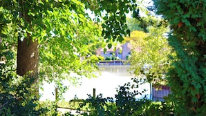 A serene lakeside view with dense foliage and a distant building. - Near Detroit Metro Area: New Baltimore Home! (New Baltimore)