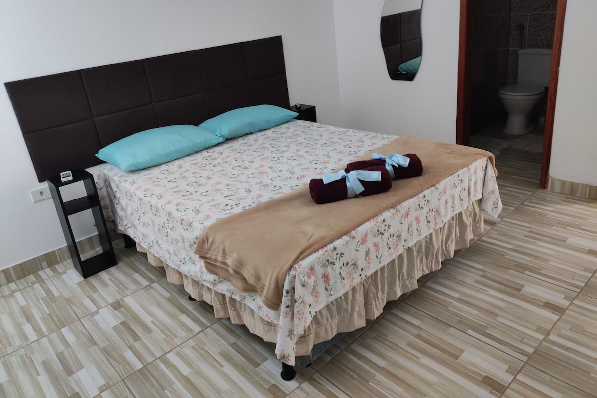 A neatly made bed with a floral bedspread, a brown throw blanket, and two towels with blue ribbons.