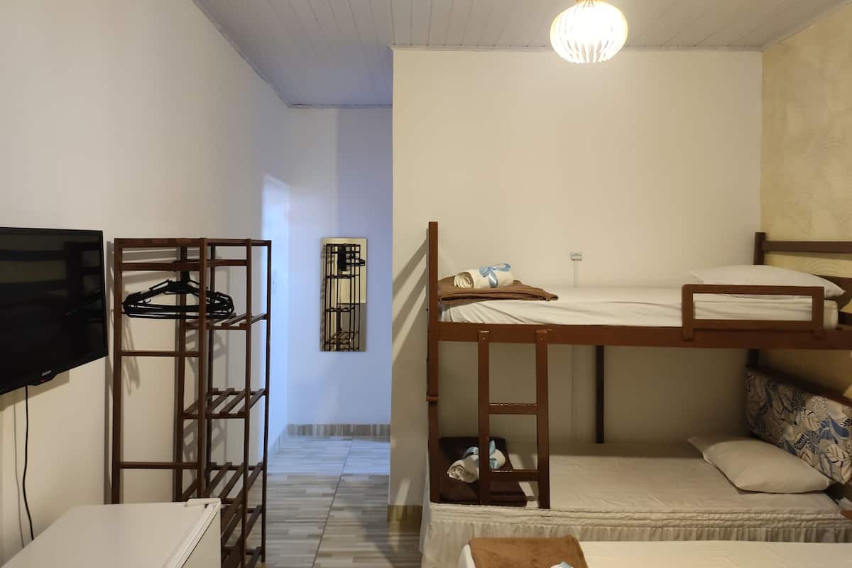 A room with a bunk bed, a TV, a wooden shelf, and a hanging light fixture.