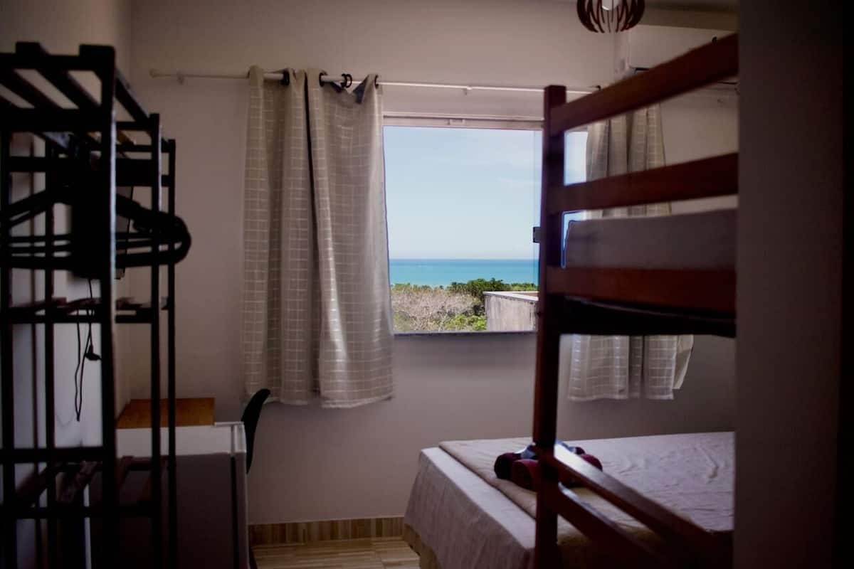 A room with a bunk bed, a window with curtains, and a view of the sea.
