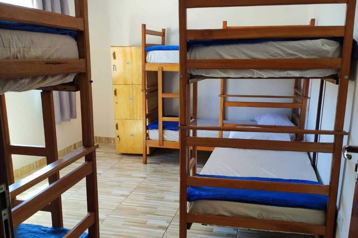 A dormitory room with bunk beds, a wooden wardrobe, and a tiled floor.