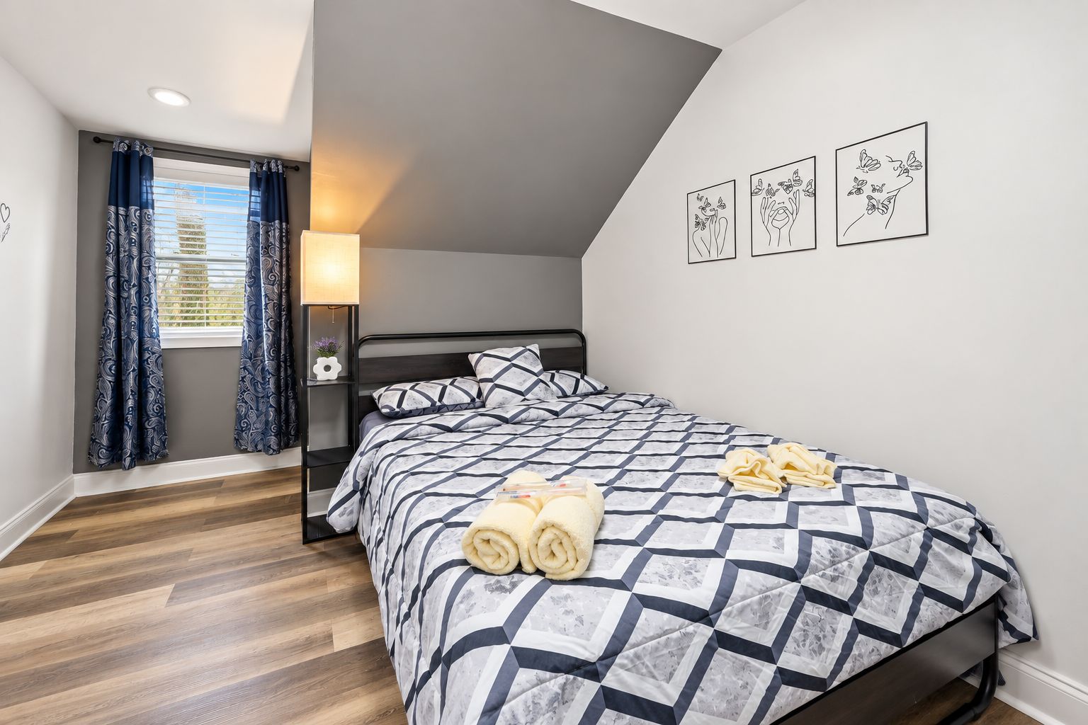 A bedroom with a bed, a nightstand, a lamp, and a window with curtains.