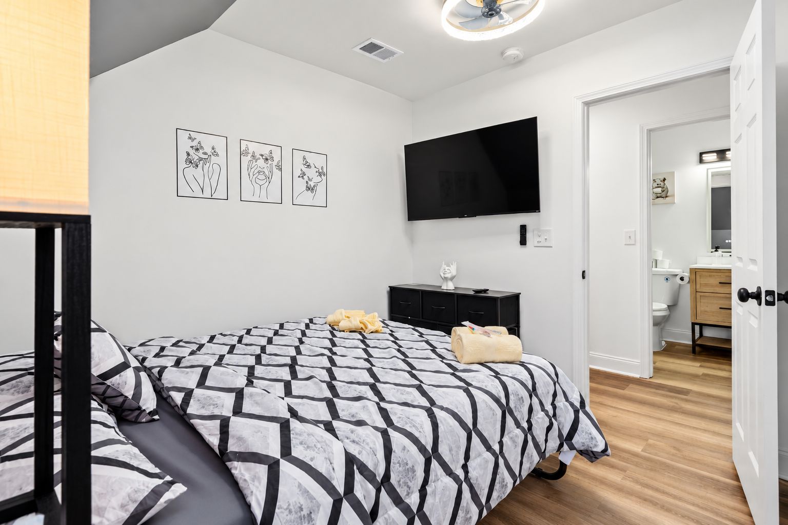 A bedroom with a bed, a flat-screen TV, a dresser, and a bathroom visible through an open door.