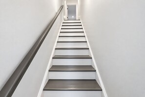 A straight staircase with a handrail on the left and a door at the top.