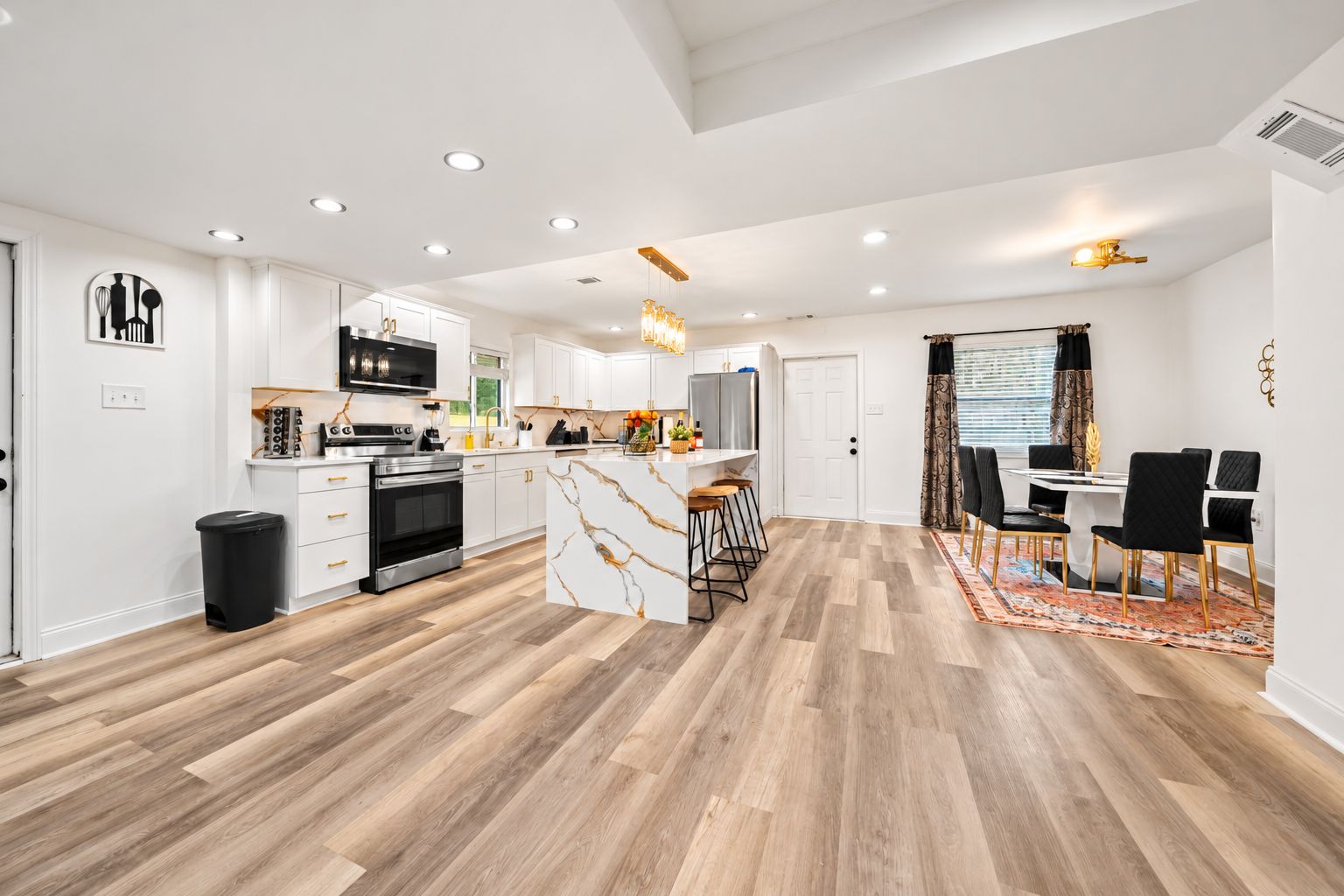 A modern kitchen with white cabinetry, a central island, and a dining area with a table and chairs.