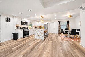 Una cuina moderna amb armaris blancs, una illa central i una zona de dinar amb taula i cadires.