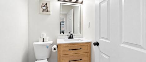 Een compacte badkamer met toilet, wastafel, spiegel en een houten kastje.