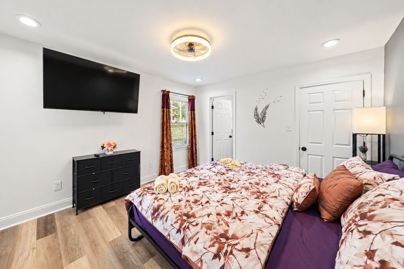 Une chambre à coucher moderne, équipée d’un lit, d’une commode, d’un téléviseur et d’un ventilateur de plafond.