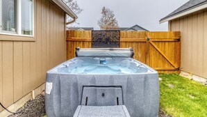 A hot tub in a backyard with a wooden fence and a house in the background. - Heart of Sisters Suite (Sisters)