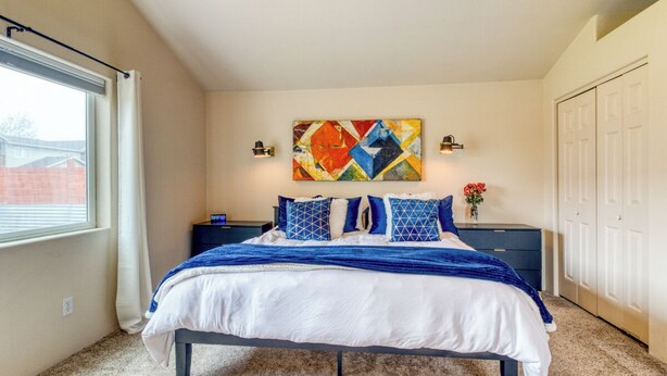 A bedroom with a bed, a nightstand, a wall-mounted lamp, a colorful abstract painting, and a closet. - Heart of Sisters Suite (Sisters)