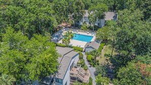 An aerial view of a resort with a swimming pool surrounded by lush greenery and a building with a curved roof. - 34 Forest Gardens: Walk to Beach, Pool, Free Bikes (Hilton Head Island)