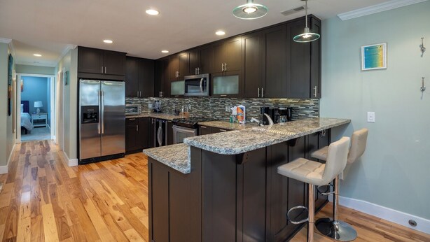 A modern kitchen with dark cabinetry, granite countertops, stainless steel appliances, and a bar area with stools. - 34 Forest Gardens: Walk to Beach, Pool, Free Bikes (Hilton Head Island)