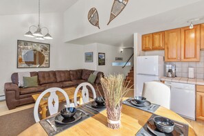 A modern living room with a brown leather sofa, white chairs, a dining table set with black bowls and chopsticks, and a vase of dried plants. - 6 Bd, 5 Ba Telluride Condos on the River Trail, Connected, Sleeps 16 (Telluride)
