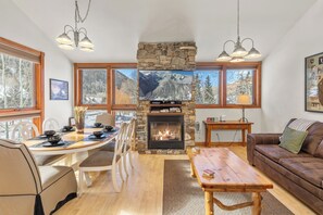 A cozy living room with a stone fireplace, wooden furniture, and large windows offering mountain views. - 6 Bd, 5 Ba Telluride Condos on the River Trail, Connected, Sleeps 16 (Telluride)