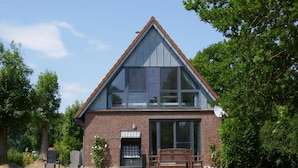 A two-story brick house with large windows, a front porch with a bench, and a satellite dish. - Ferienhaus in Fehmarn OT Kopendorf (Fehmarn)